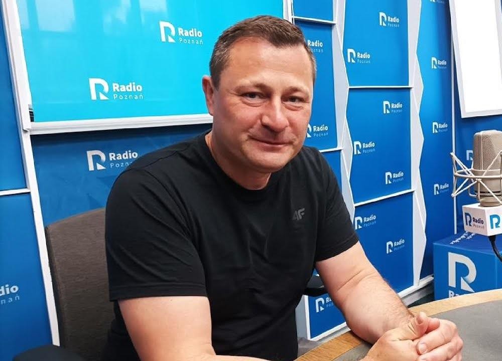 Krzysztof Paszyk podczas wystąpienia publicznego, gestykulujący i uśmiechnięty, w tle zamazane elementy politycznego wydarzenia.