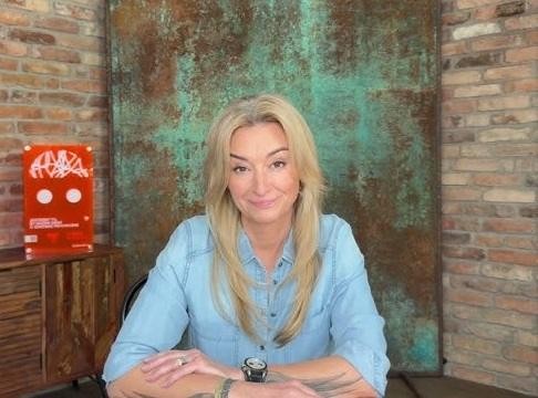 Martyna Wojciechowska podczas podróży, otoczona dziećmi, uśmiechnięta, w tle egzotyczny krajobraz.