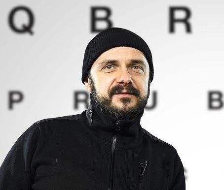 Arkadiusz Jakubik, wokalista zespołu Dr Misio, na scenie podczas koncertu, trzymający mikrofon, z ekspresyjnym wyrazem twarzy.