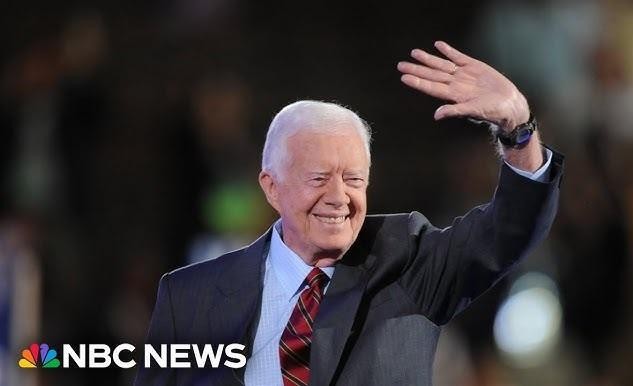 Jimmy Carter w roboczym ubraniu i kasku, aktywnie budujący dom dla Habitat for Humanity, uśmiechający się i współpracujący z innymi wolontariuszami.