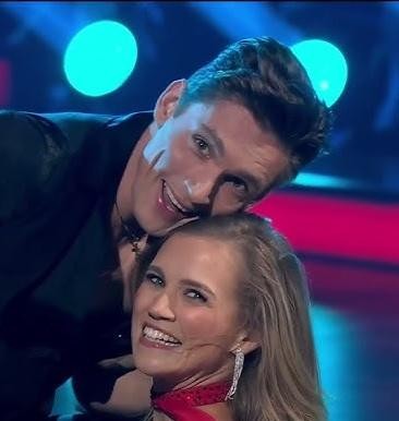 Agnieszka Kaczorowska uśmiechnięta, z czułością trzymająca swoje dwie małe córki, Emilię i Gabrielę, w ciepłej, rodzinnej scenerii.