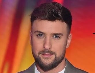 Aleksander Sikora, polski prezenter telewizyjny, w dynamicznej pozie, uśmiechnięty, w studiu telewizyjnym.