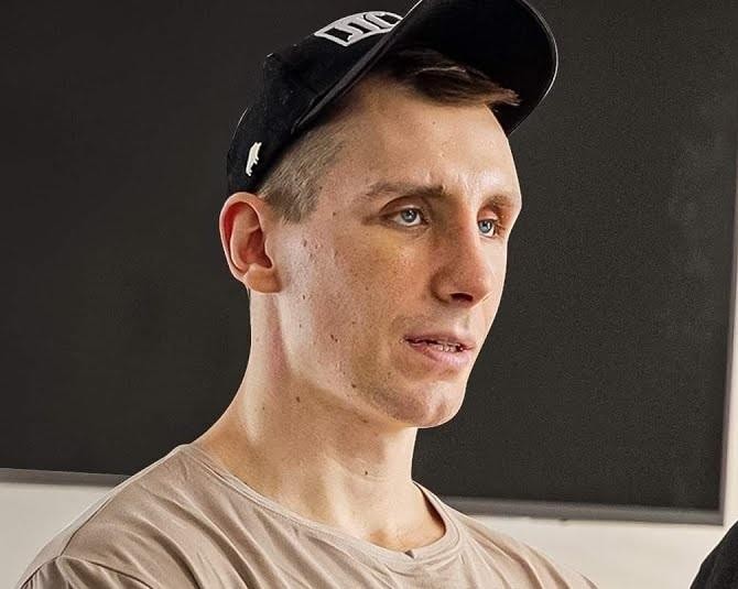 Michał Owczarzak (Owca WK) wykonujący martwy ciąg z dużym ciężarem, skupiony i muskularny, w tle zamazane wyposażenie siłowni.