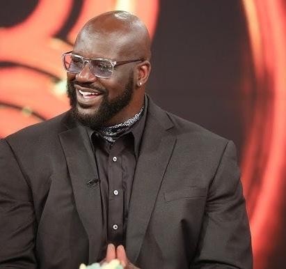 Shaquille O'Neal w akcji na boisku w koszulce Miami Heat, wykonujący dynamiczny ruch lub wsad, ukazujący jego siłę i atletyzm.