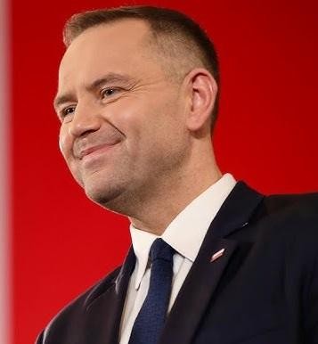 Karol Nawrocki podczas wydarzenia historycznego, z pasją przemawiający lub odsłaniający tablicę pamiątkową, podkreślający jego rolę w upamiętnianiu historii.