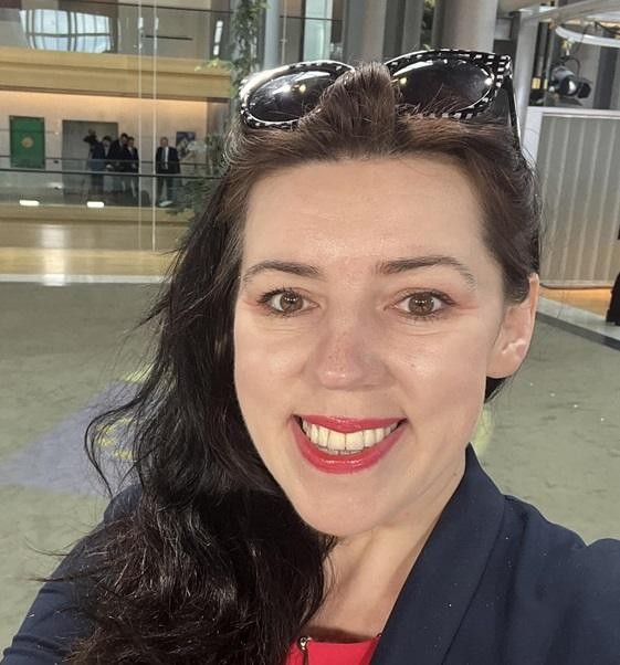 Dominika Ćosić, dziennikarka i pisarka, w otoczeniu książek lub map, symbolizujących jej intelektualne i geograficzne zainteresowania.
