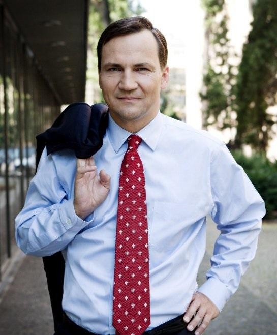 Radosław Sikorski przemawiający z mównicy, z mikrofonem, w tle rozmyta sala konferencyjna, ukazujący jego zaangażowanie w debatę publiczną.
