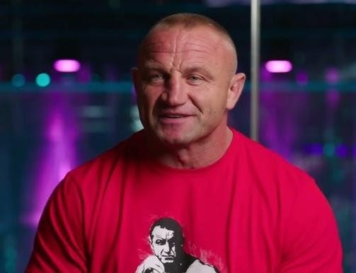 Mariusz Pudzianowski w trakcie walki MMA w oktagonie, ukazujący dynamikę i siłę uderzenia.