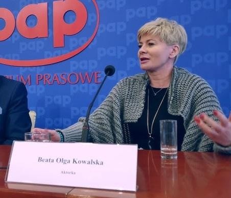 Beata Olga Kowalska na scenie teatralnej w pełnej kadrze, w eleganckim kostiumie scenicznym, w dynamicznej pozie oddającej jej energię i wszechstronność aktorską.