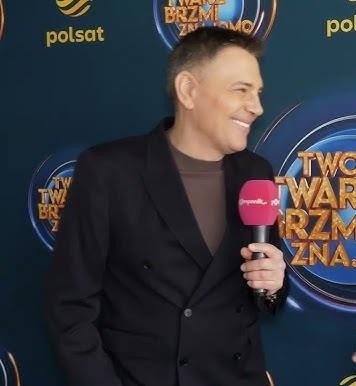Krzysztof Ibisz w interakcji z publicznością lub współpracownikami, ukazujący swoją charyzmę i zaangażowanie.