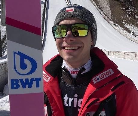 Alt: Jakub Wolny podczas treningu skoków narciarskich, skupiony na przygotowaniu do skoku.